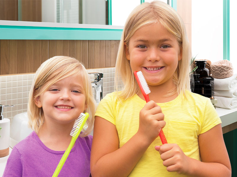 Two young girls holding giant toothbrushes.